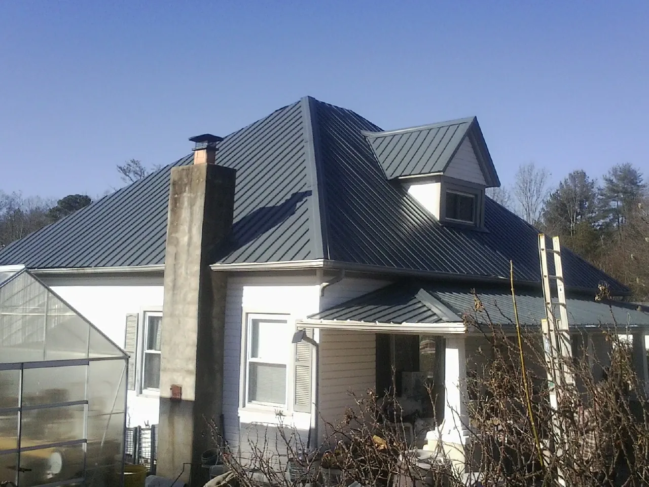 Dark blue standing seam metal roof on a white farmhouse with dormer — Slate & Tile Roof Repair by Roofing Brothers in Jay Em