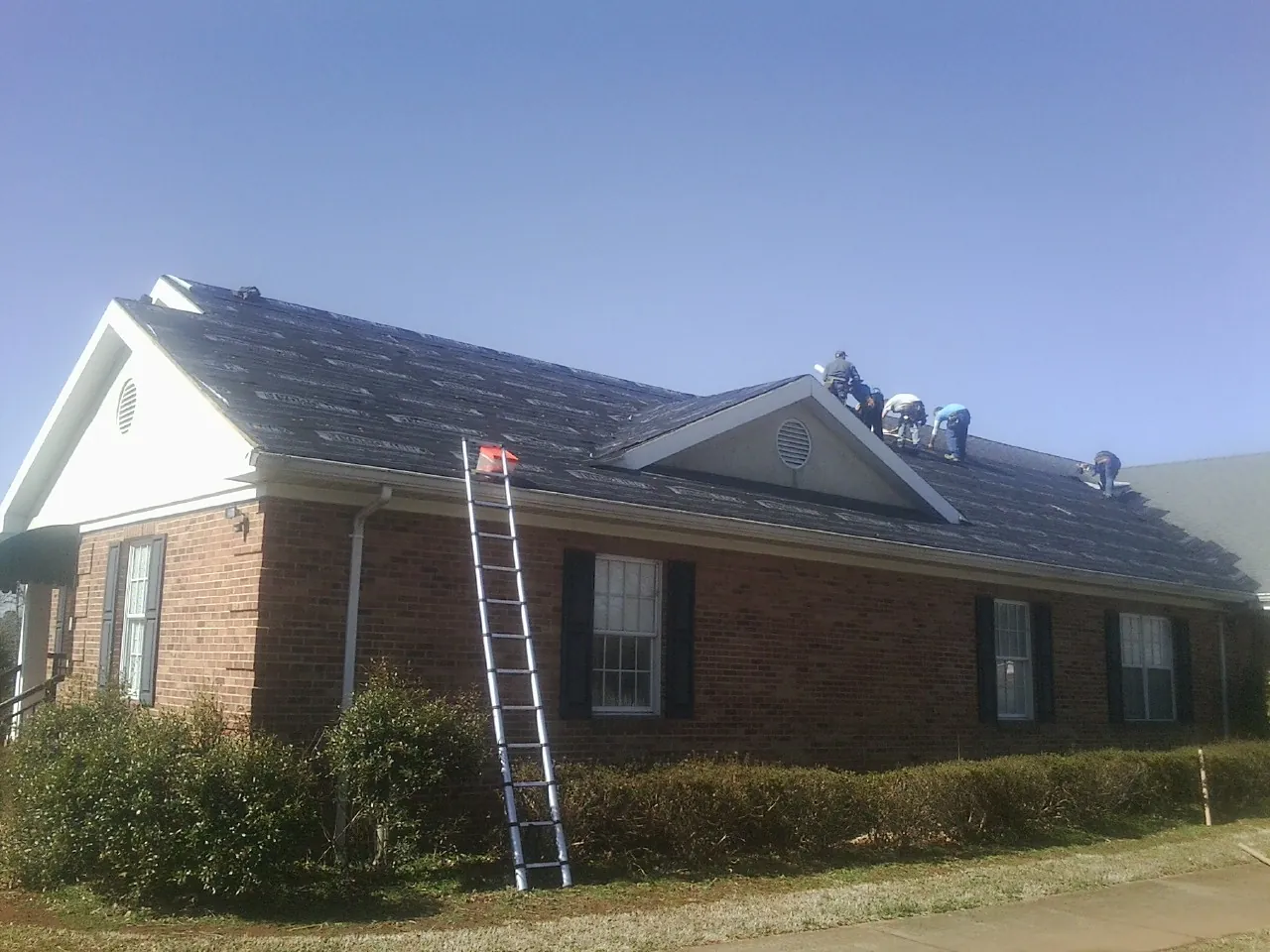 Crew tearing shingles off a brick ranch roof with a ladder set — Emergency Roof Repair work by our crew in Jay Em
