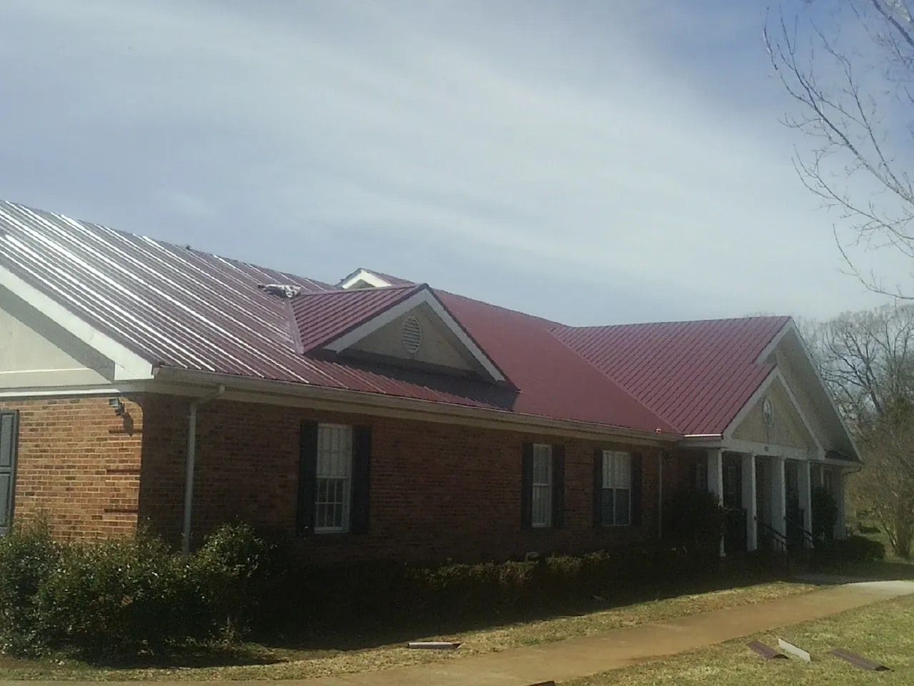 Red metal roof with gabled entries on a long brick building, from a Hail Damage Roof Repair job in Jay Em