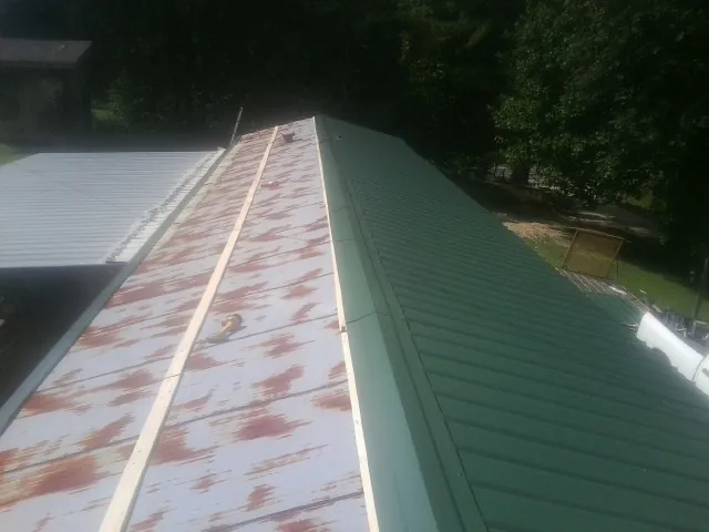 Old rusted panels beside newly installed green metal roofing — Wind Damage Roof Repair by Roofing Brothers in Jay Em