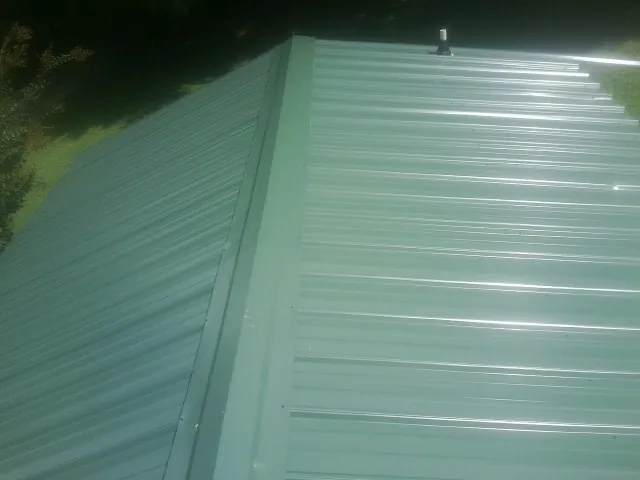 New green metal panels meeting at the ridge of a roof — Flat Roof Repair work by our crew in Jay Em