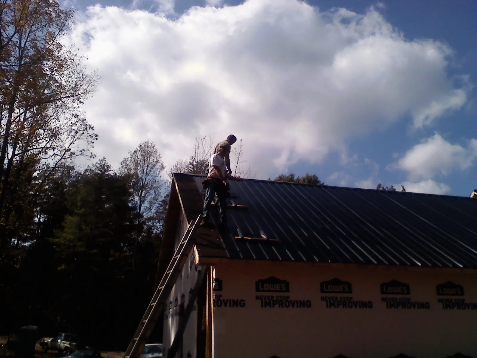 Roofer fastening dark metal panels high against a cloudy sky, from a Roof Inspection job in Jay Em