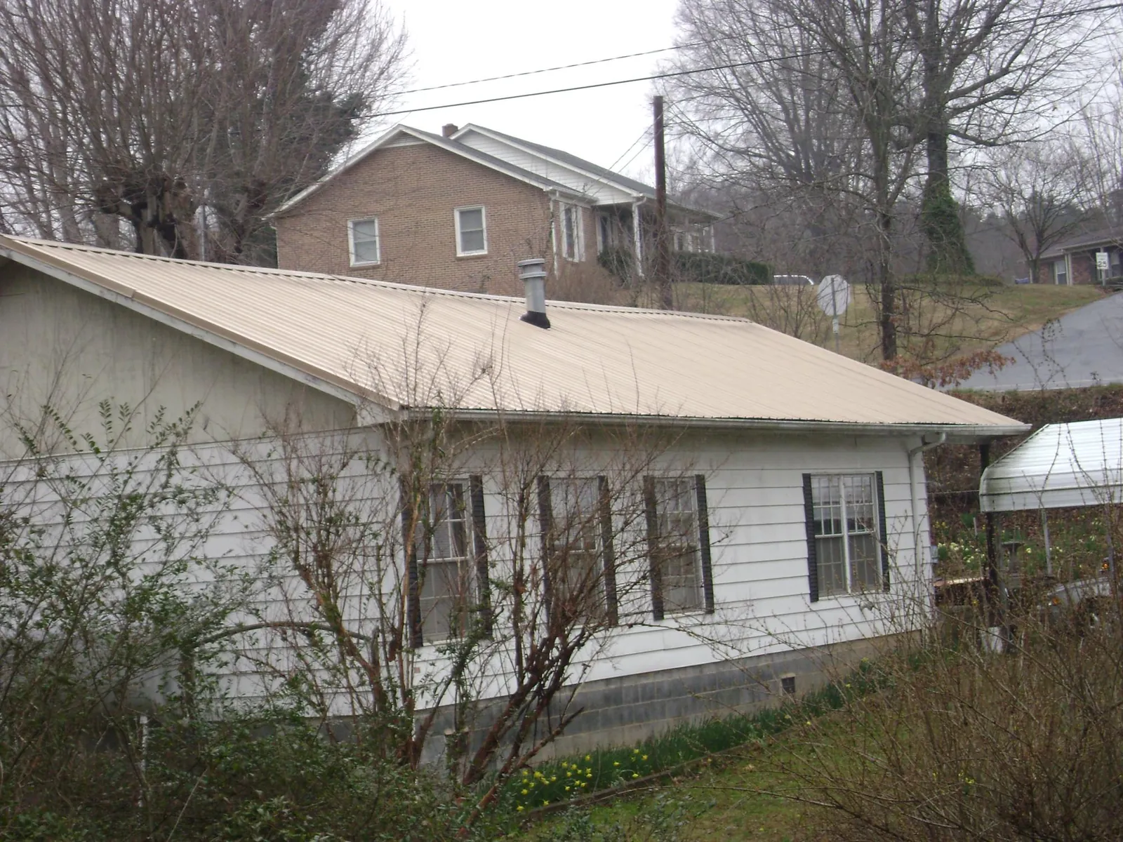 Tan metal roof on a white sided house set into a hillside — Commercial Roofing by Roofing Brothers in Jay Em