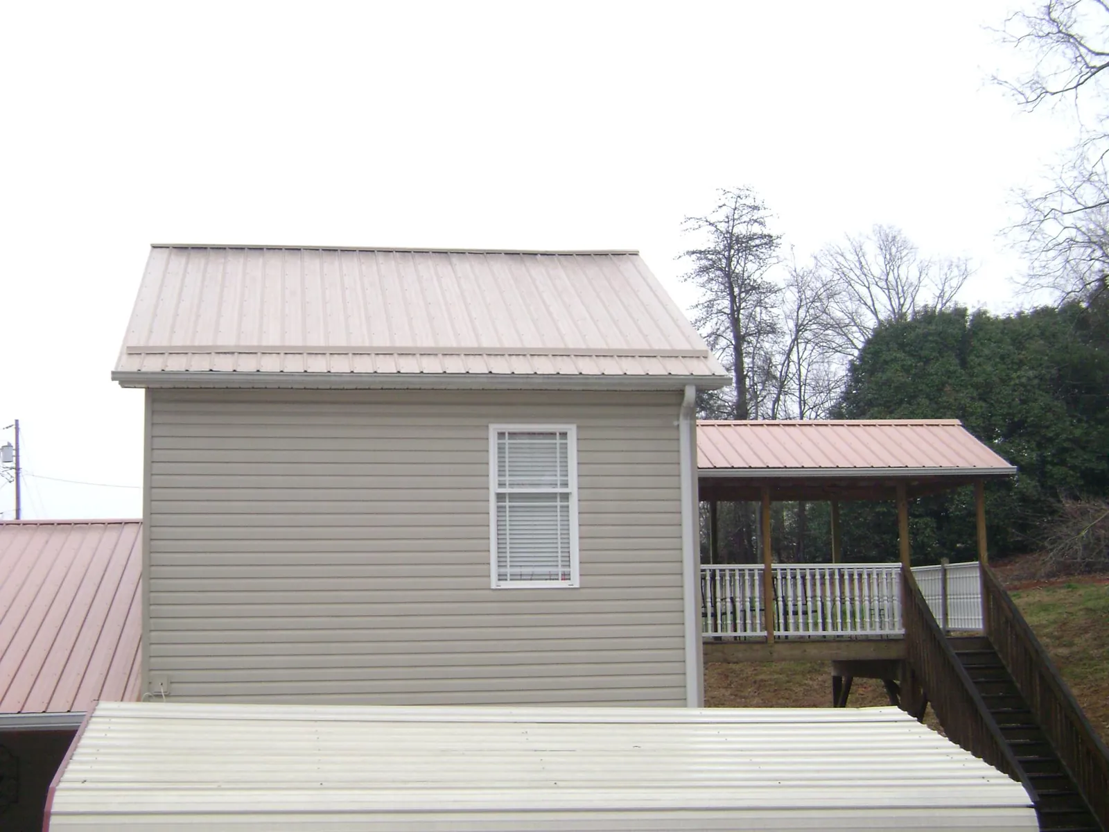Tan metal roofs on a two story addition and attached porch, from a Roof Replacement job in Jay Em