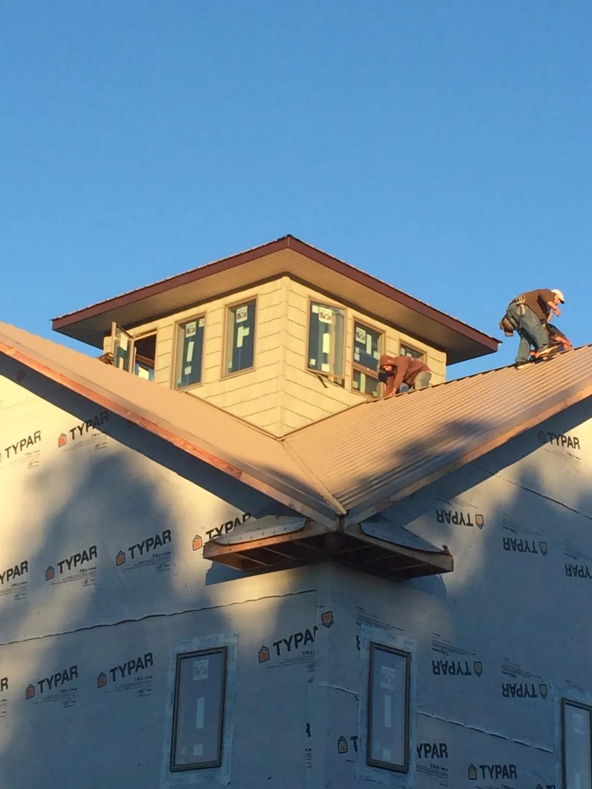 Roofers working around a rooftop cupola on a new metal roof at sunset — Roof Waterproofing in Jay Em by Roofing Brothers